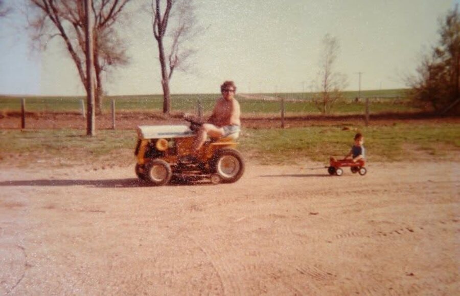 Young Garrett McClure being pulled in a wagon by his dad's tractor on the farm