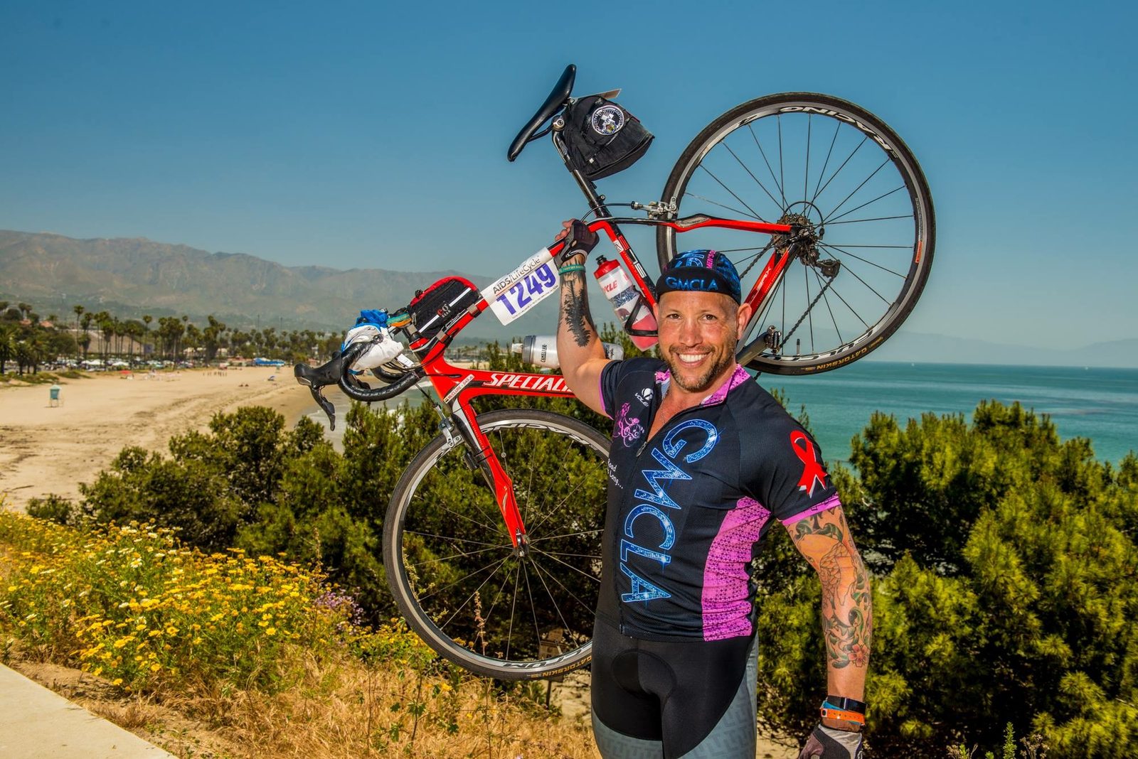 Garrett McClure on AIDS/LifeCycle in his Gay Men's Chorus of LA team jersey, holding his bike on the Santa Barbara coast
