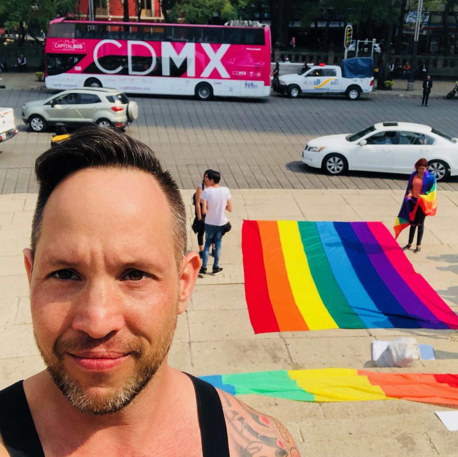 Garrett McClure at Pride in Mexico City with a rainbow flag and a CDMX bus behind him